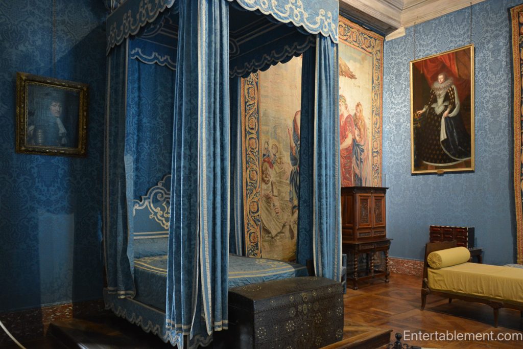 Blue-upholstered four-poster bed with draped canopy surrounded by tapestry-covered walls
