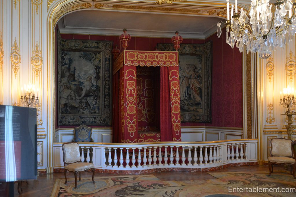 Opulent bed framed in red and gold fabric with a balustrade enclosure and gilded decor