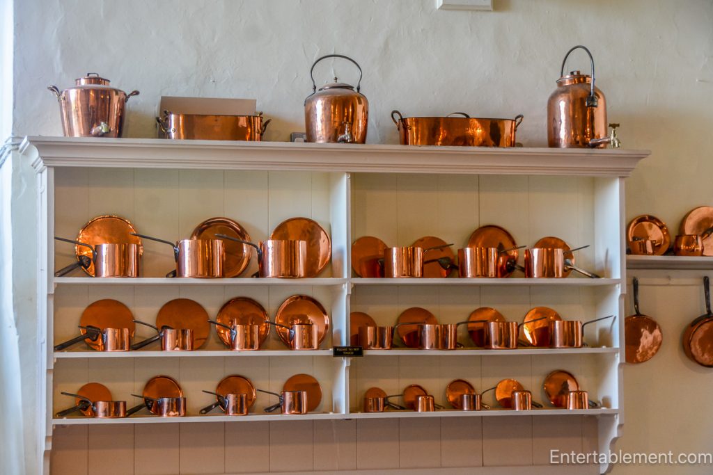 Restored Victorian kitchen at Hardwick Hall featuring a large hearth, copper pots, and traditional cooking implements.