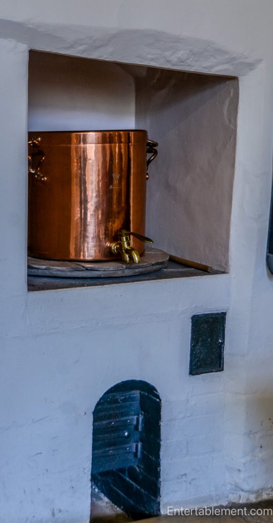 Restored Victorian kitchen at Hardwick Hall featuring a large hearth, copper pots, and traditional cooking implements.