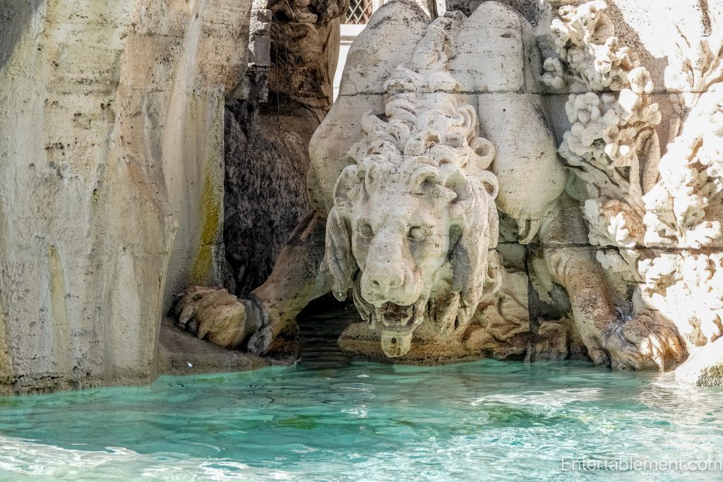 Close-up of a carved stone lion spouting water into a turquoise fountain pool in Piazza Navona, Rome.