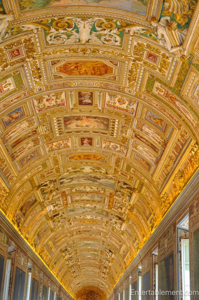 Ornate barrel-vaulted ceiling richly decorated with frescoes, stucco figures, and gold detailing inside the Vatican Museums in Rome.