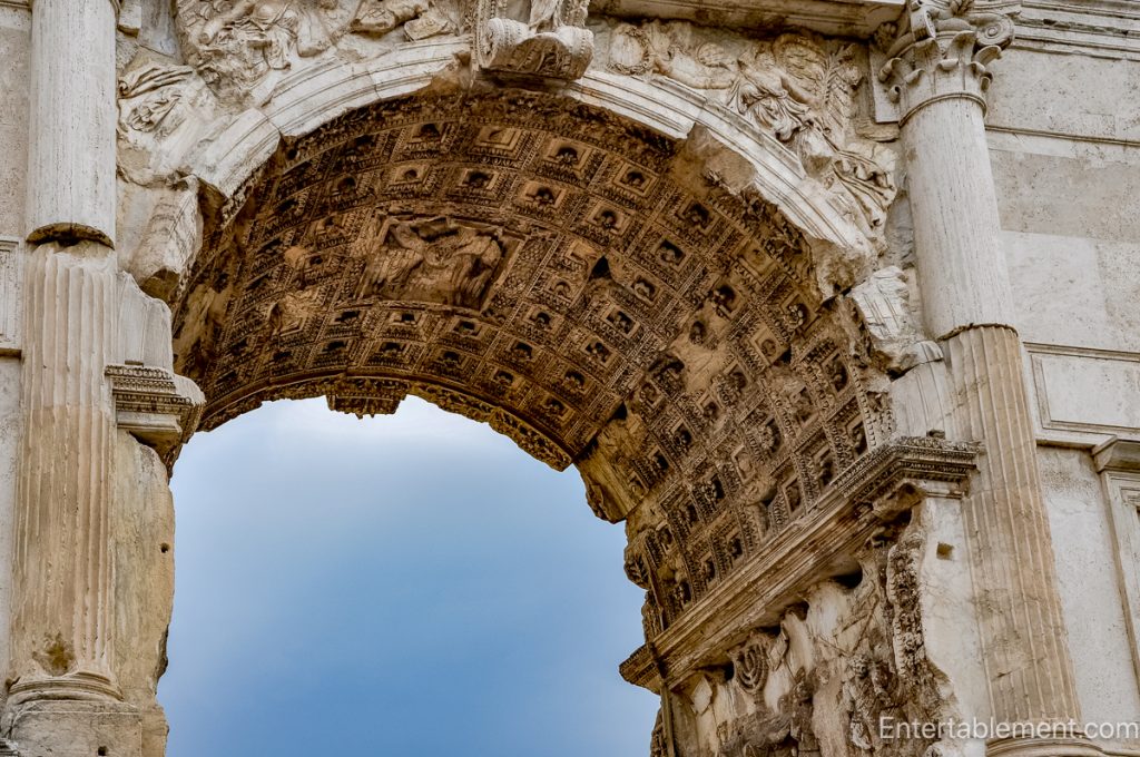 Close-up view through a triumphal arch with a richly carved coffered ceiling and sculpted stone details in Rome.