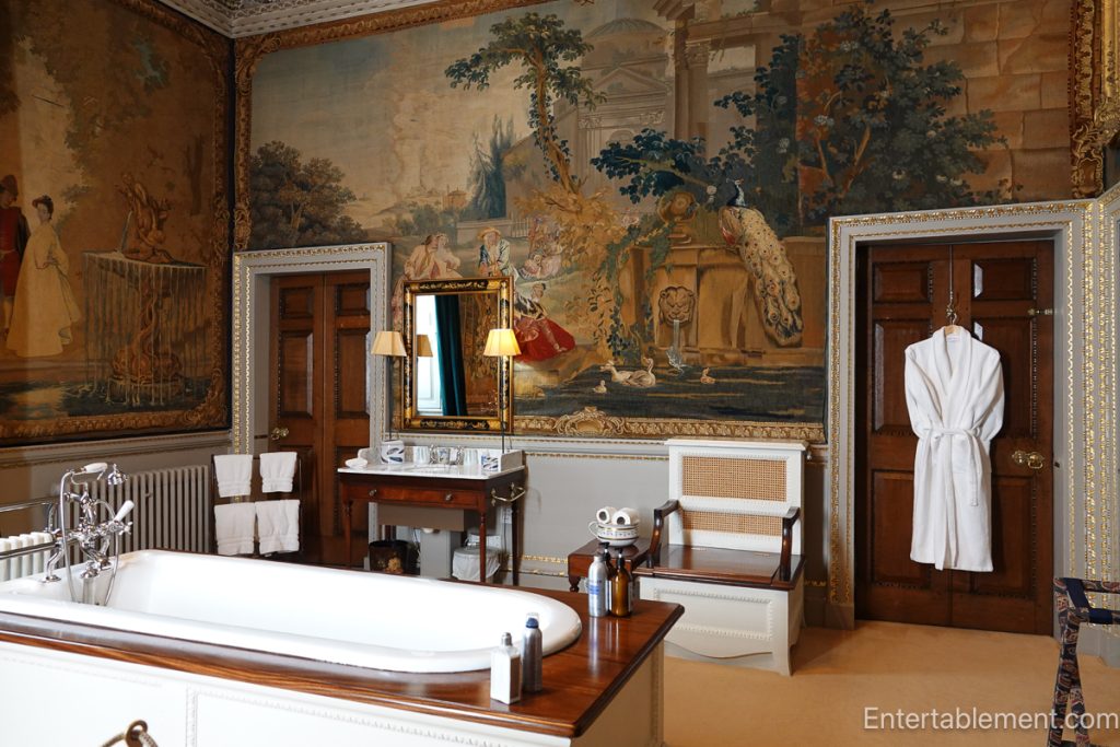 Historic bathroom at Holkham Hall with tapestries covering walls and freestanding tub
