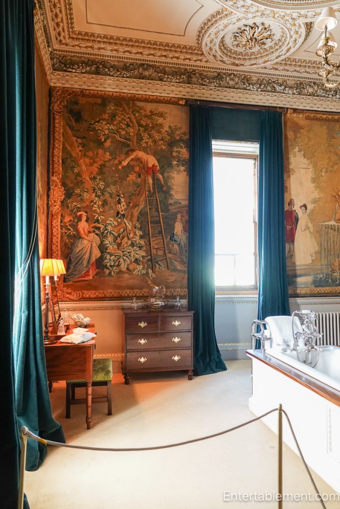 Historic bathroom at Holkham Hall with tapestries covering walls and freestanding tub