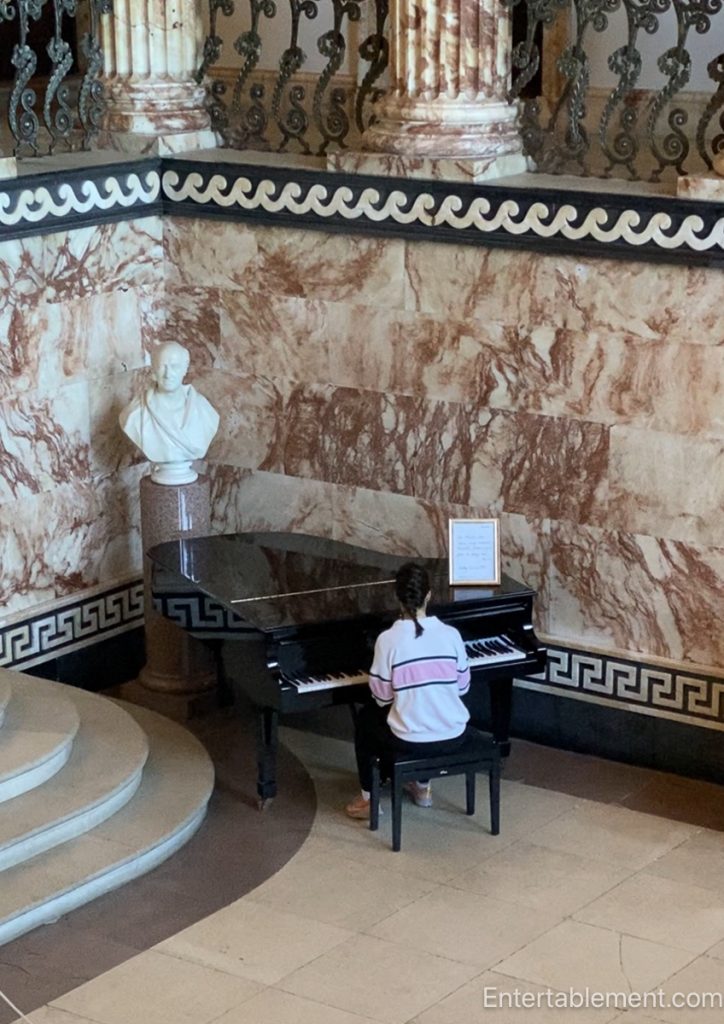 Young girl playing piano in the Marble Hall at Holkham, surrounded by marble walls and classical detail
