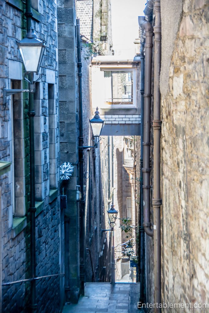 Narrow stone passageway in Edinburgh’s Old Town, with traditional lanterns and a bridge connecting buildings overhead
